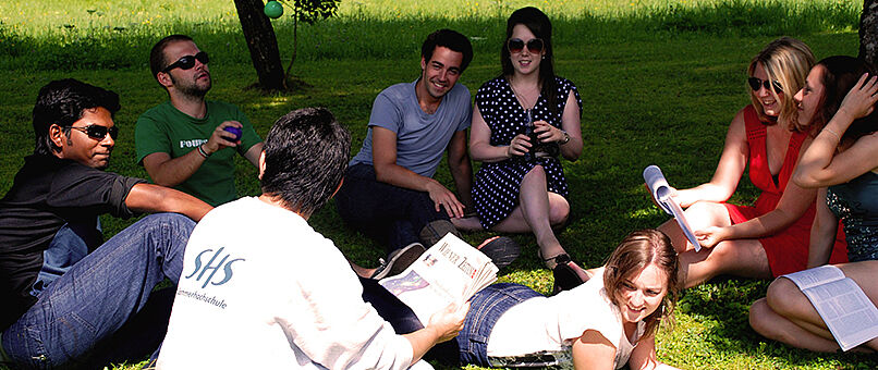 Students sitting in a circle on the meadow, laughing and studying.